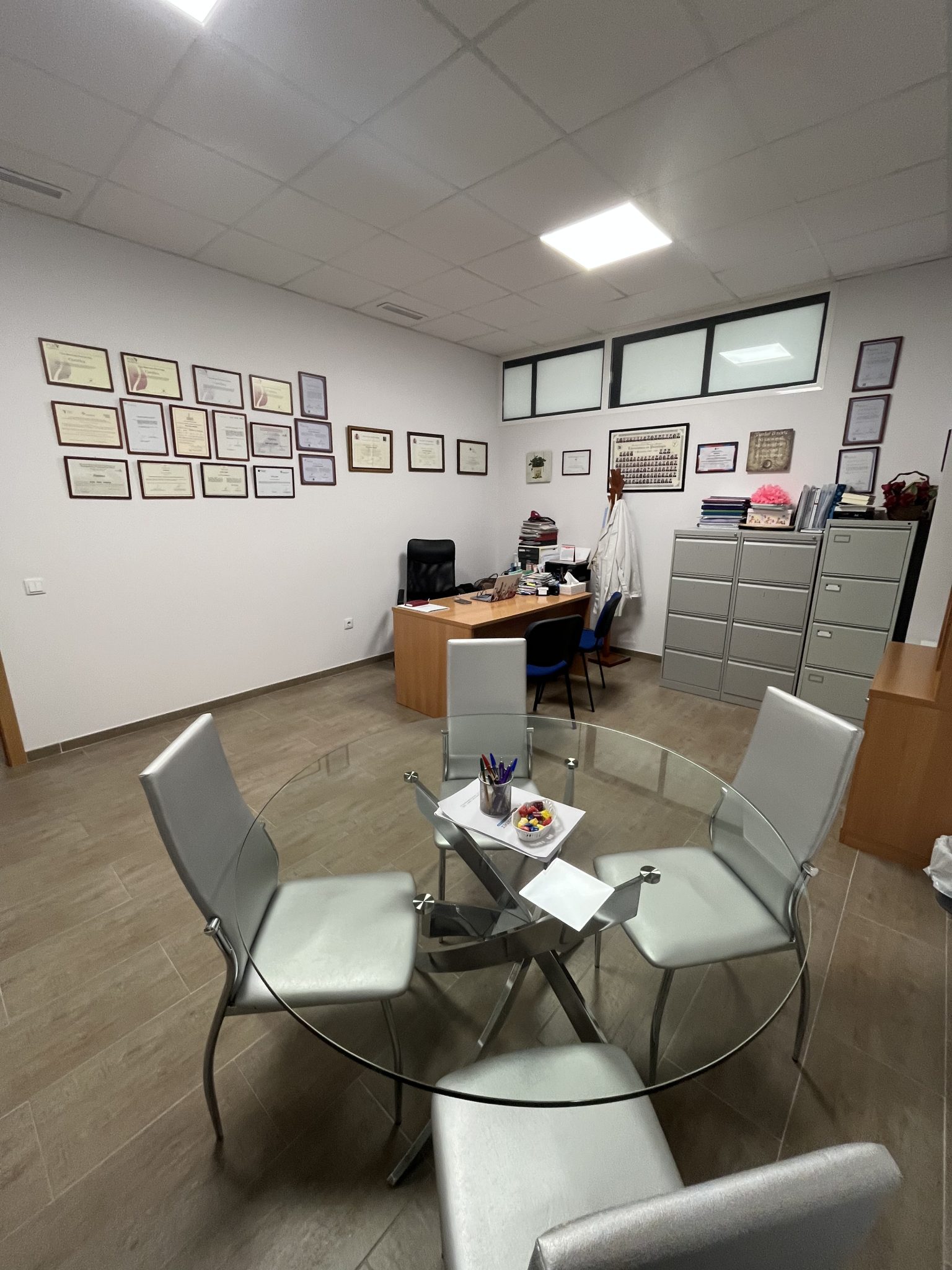 Oficina con mesa de cristal y certificados en las paredes